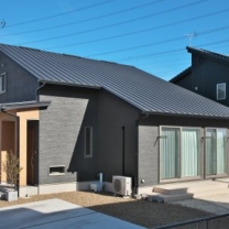 平屋かと思わせる片流れの大屋根と黒い外壁が特徴の外観。玄関まわりはナチュラルな木目調を選んで変化を付けた。